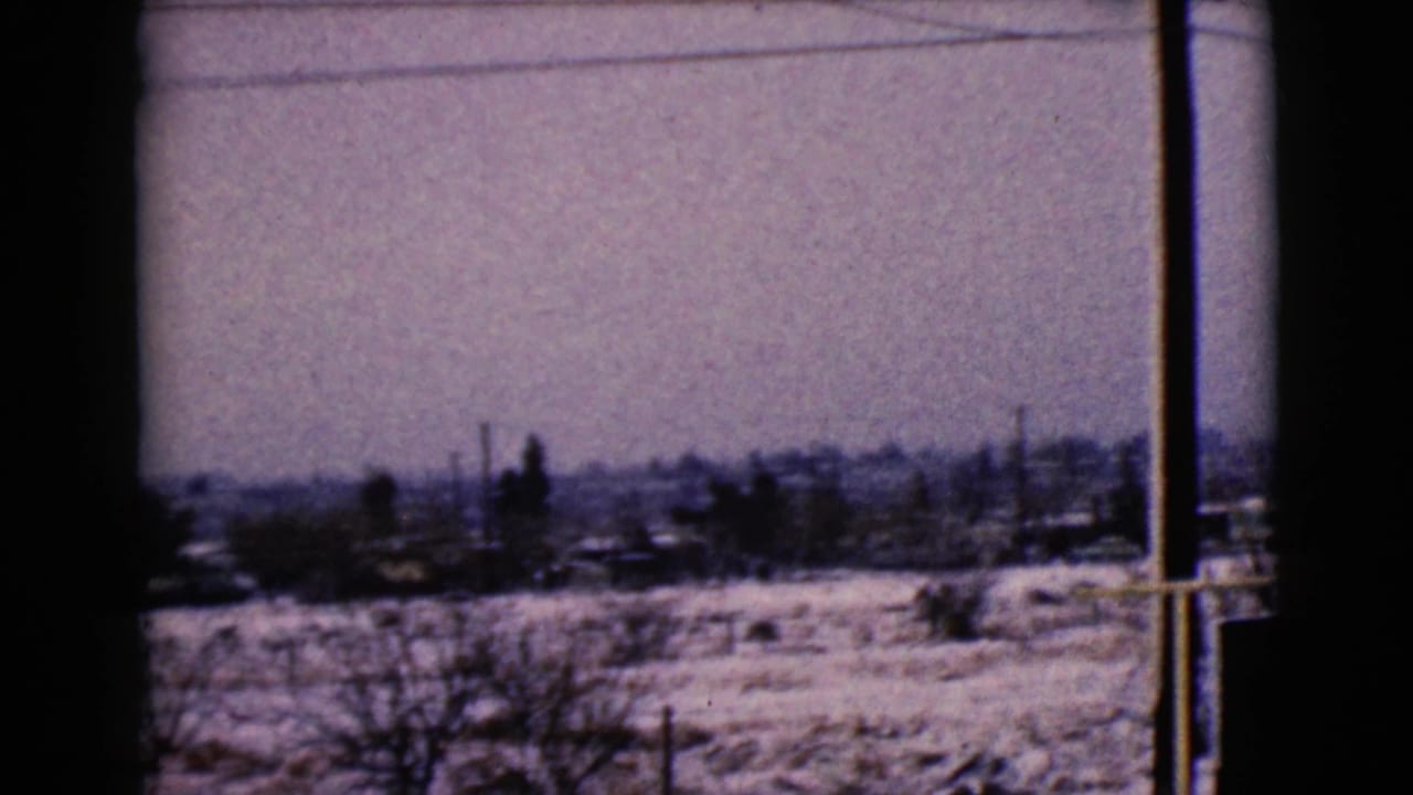 Snowy Clarksdale, Arizona exurban view on 8mm film, with low houses, bare trees, utility poles, and a dark window divider.