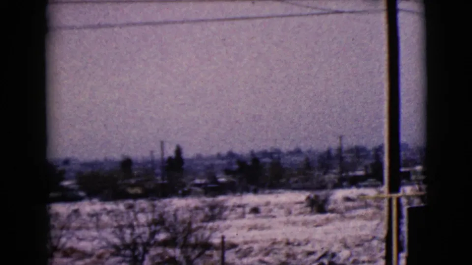 Snowy Clarksdale, Arizona exurban view on 8mm film, with low houses, bare trees, utility poles, and a dark window divider.