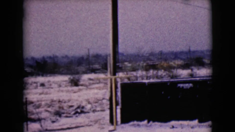 1968 8mm frame showing a dark dumpster or large container below a snowy Clarksdale landscape with distant homes and bare trees.
