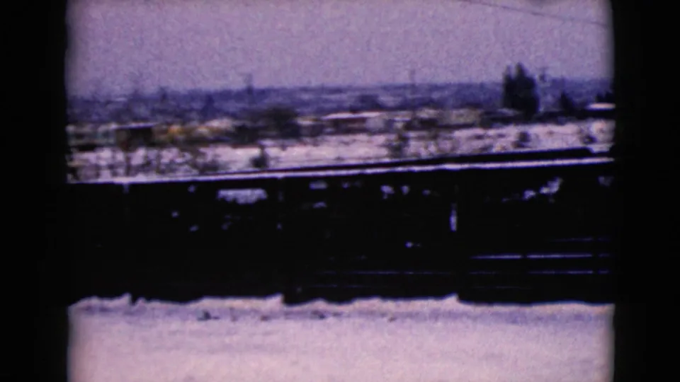 Snowy Clarksdale, Arizona home-movie view with a dark foreground dumpster or container, leafless trees, utility poles, and distant houses.