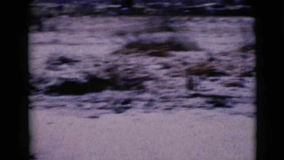 1968 home-movie frame of snow-covered ground in Clarksdale, Arizona, with blurred roadside brush and a low distant horizon.
