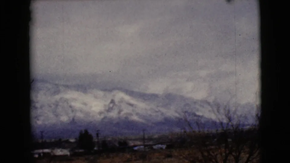 1968 8mm view near Clarksdale, Arizona, showing clouded snow-covered mountains with bare branches and a dark tree in front.