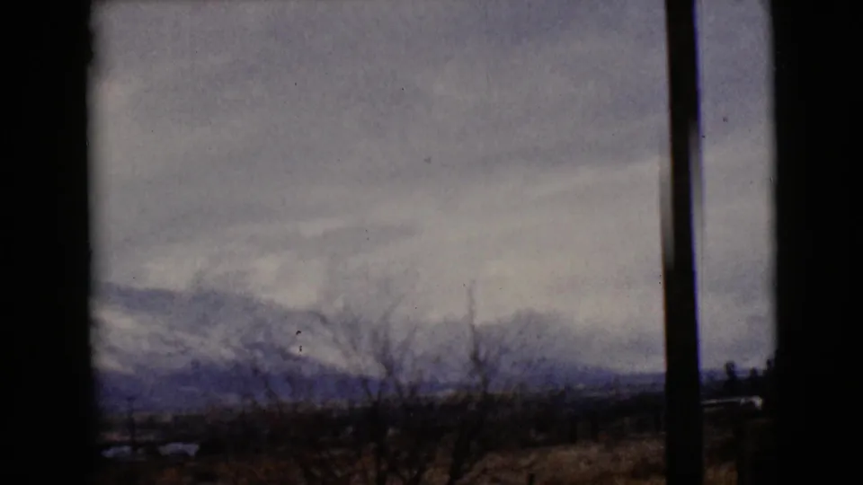 1968 8mm frame near Clarksdale, Arizona, with snowy mountains, bare winter brush, and a dark vertical film or window edge.