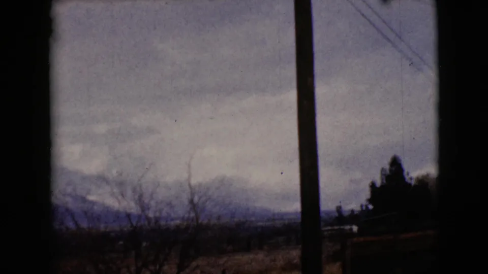 1968 8mm view near Clarksdale, Arizona, with a utility pole, bare trees and distant mountains beneath an overcast sky.