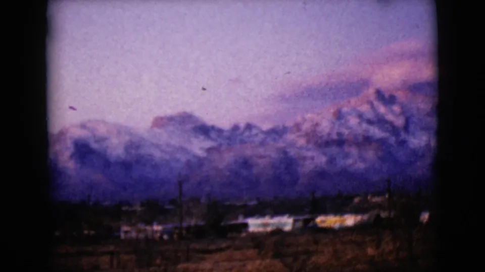 1968 8mm view near Clarksdale, Arizona, showing storm clouds over snow-dusted peaks with low structures below.