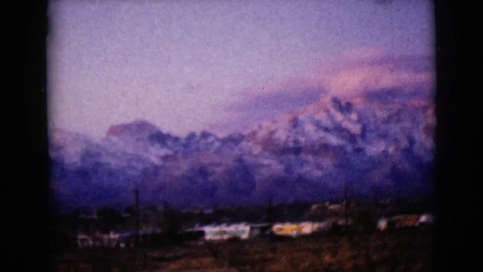 1968 8mm frame from Clarksdale, Arizona, showing snowy mountains, low buildings, and a purple-pink sky at dusk.