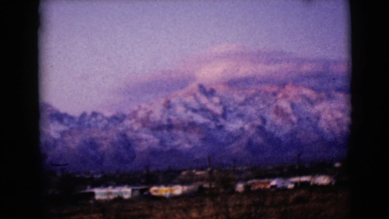 Distant snowy peaks and low town buildings beneath pink-purple clouds.