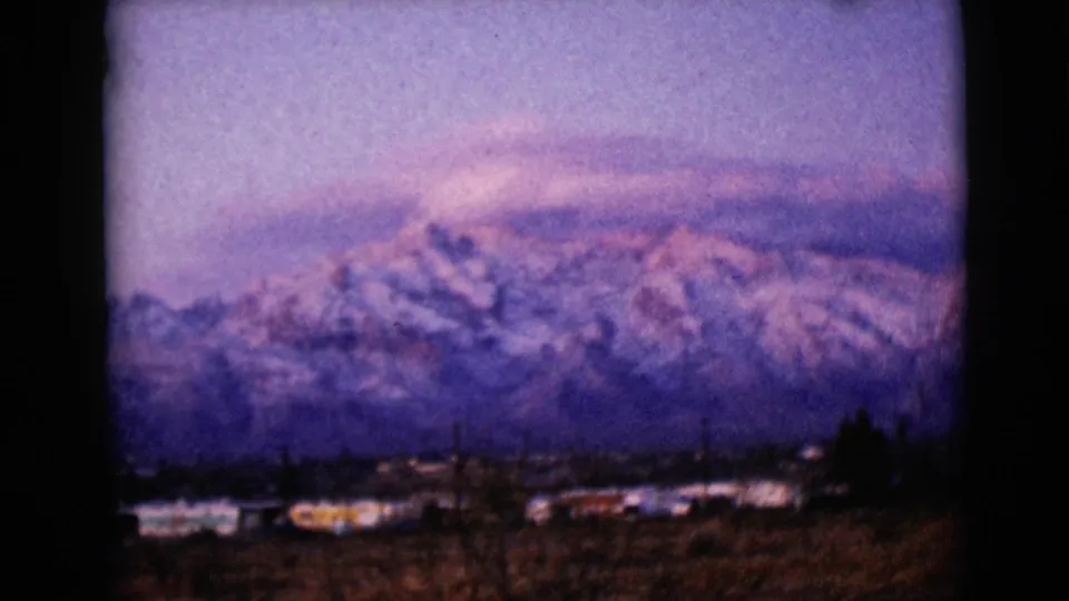 Soft 8mm footage shows a snow-covered mountain ridge above distant buildings in the stated Clarksdale, Arizona setting.