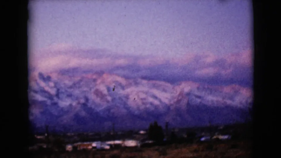 Final frame of the 1968 8mm pan shows snowy Arizona mountains, purple evening light, and a small settlement at the base.
