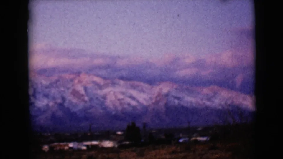 1968 8mm view near Clarksdale, Arizona, showing snow-covered mountain peaks beyond dark foreground brush at dusk.