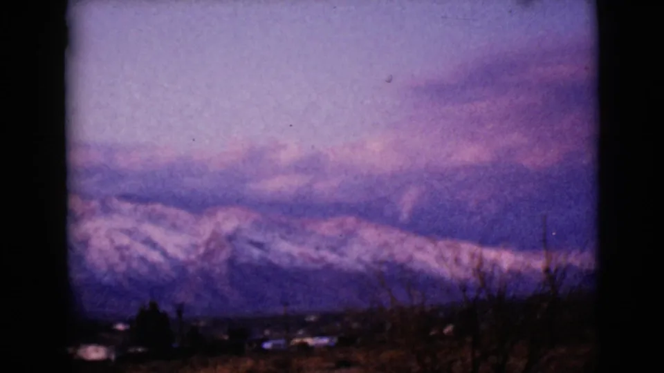 Snow-dusted mountain peaks appear beyond a dark valley foreground in this 1968 8mm Arizona home-movie frame.
