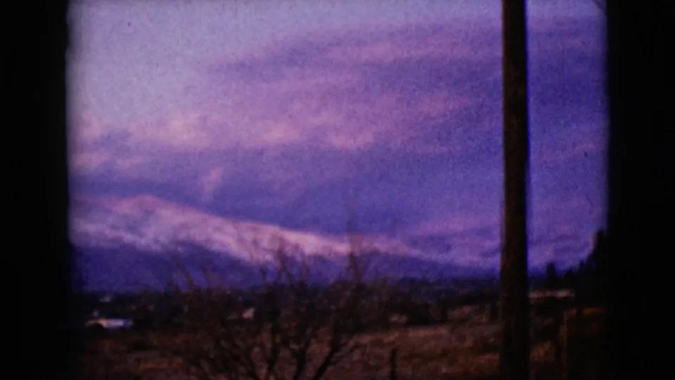 1968 8mm Arizona landscape with snowy ridges, bare foreground trees, and a utility pole silhouetted against dusk light.