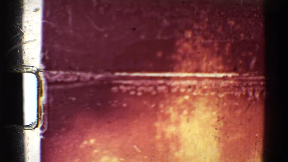 1971 Mauna Ulu 8mm frame showing film gate edges, scratches, and a bright orange lava flare against darkness.