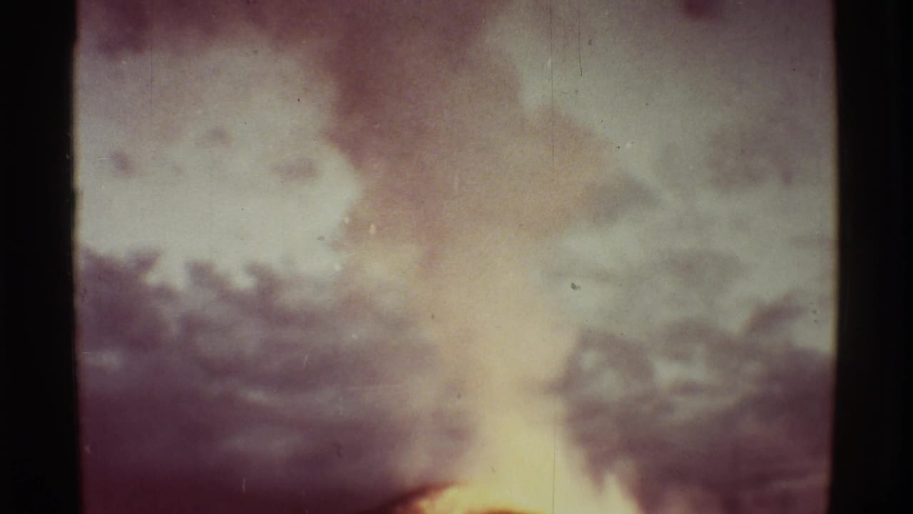 Distant volcanic plume rising under a pale sky with dark film edges.