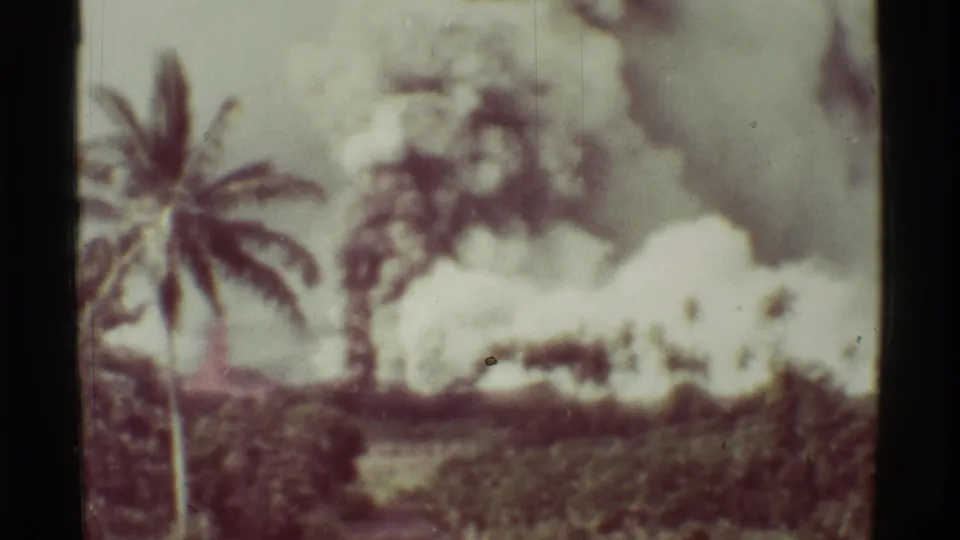 Faded 8mm frame from Mauna Ulu, Hawaii, showing a palm tree and broad eruption smoke across the landscape.