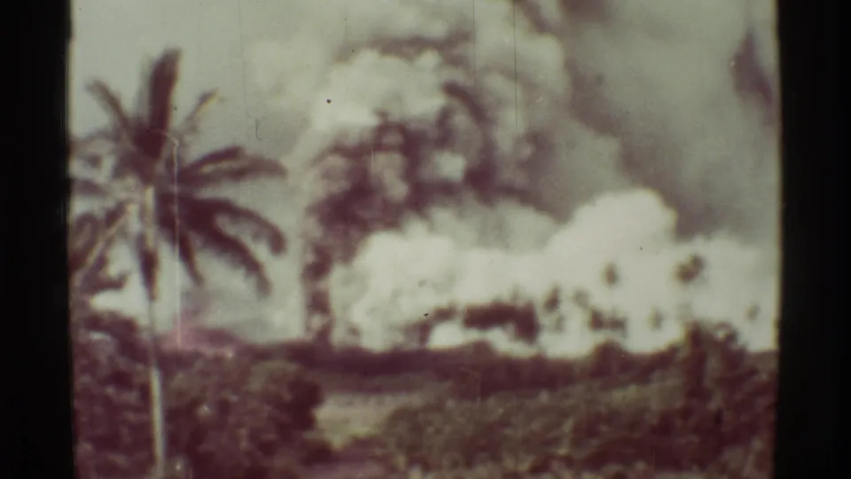 1971 Mauna Ulu home-movie still showing a palm tree at left and thick volcanic smoke rising behind vegetation.