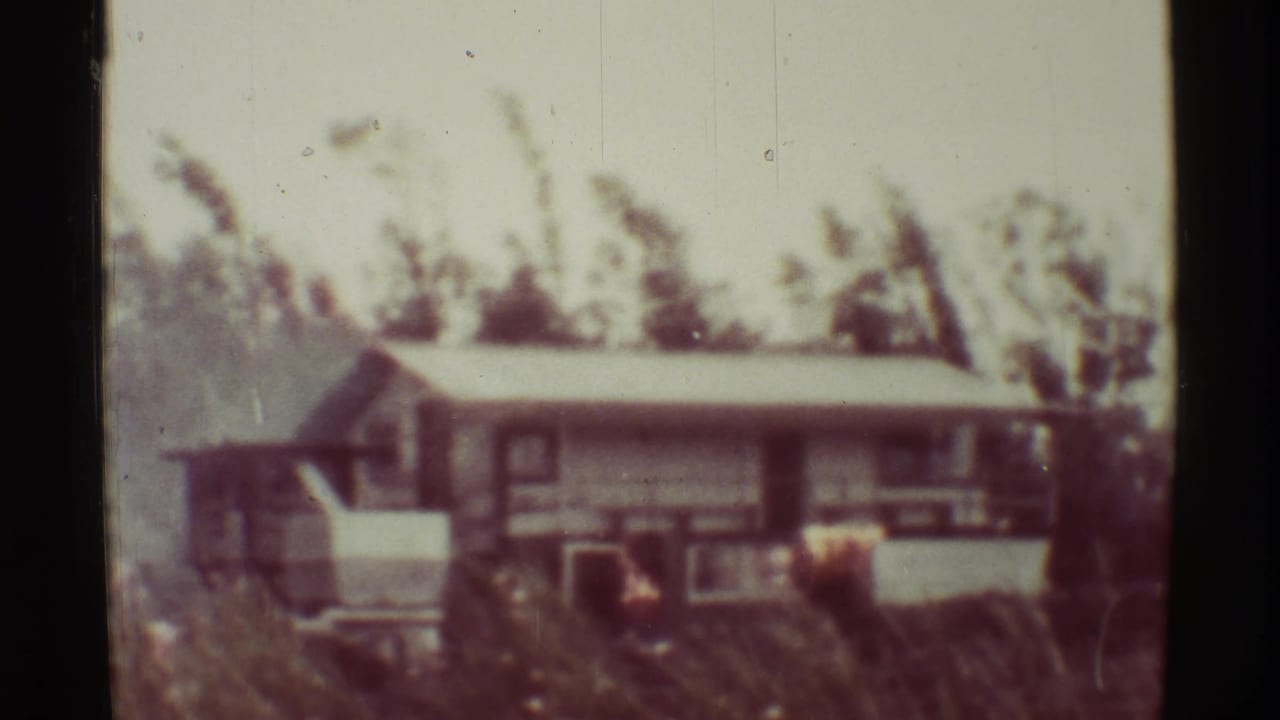 A low house with a sloped roof is seen through soft 8mm focus and dark film borders.