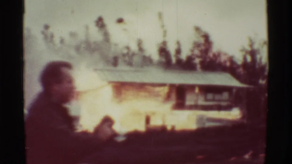 A 1971 Mauna Ulu 8mm frame shows a foreground adult silhouette near a house fire, with flames and smoke behind the figure.