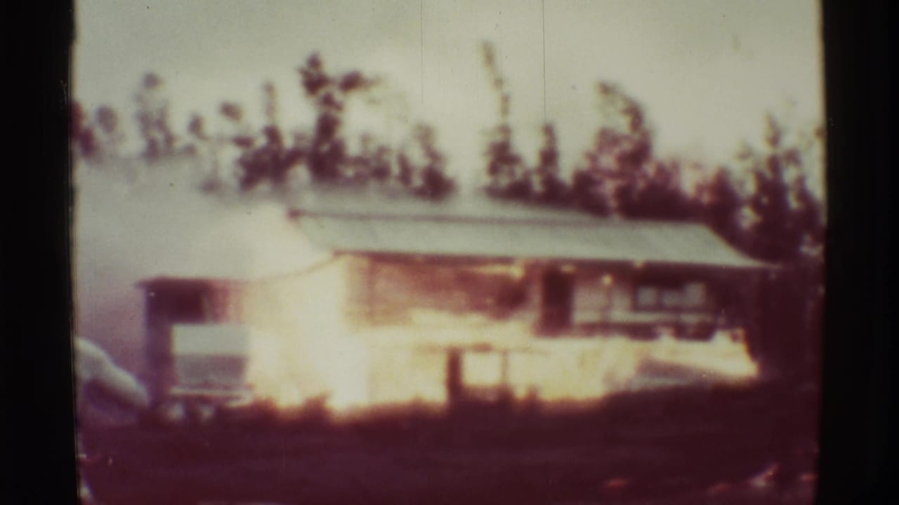 The burning structure remains visible in the 1971 Mauna Ulu footage, with fire glowing along the wall and smoke drifting through the trees.