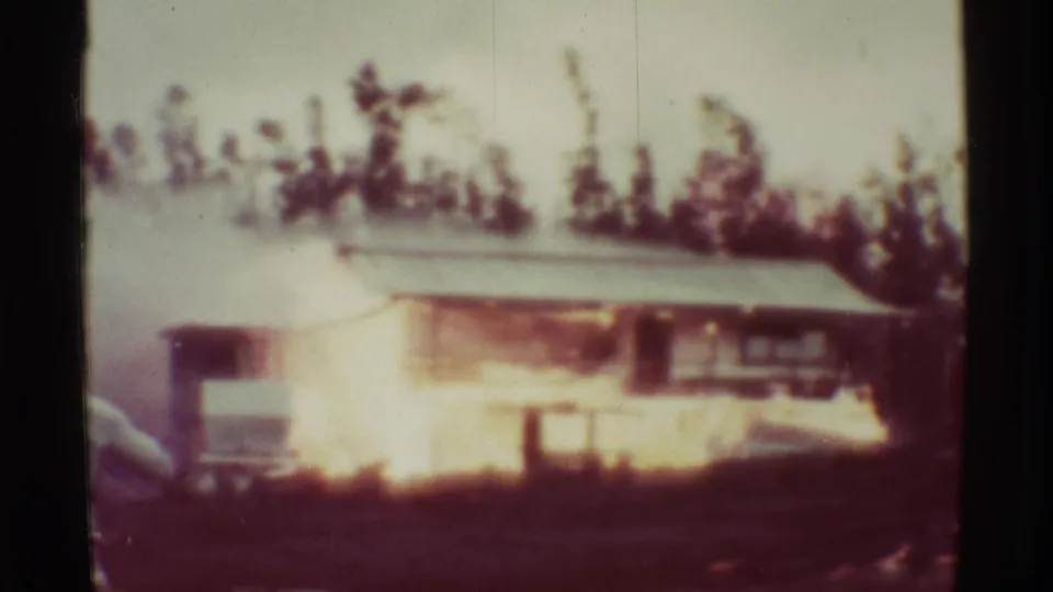The burning structure remains visible in the 1971 Mauna Ulu footage, with fire glowing along the wall and smoke drifting through the trees.