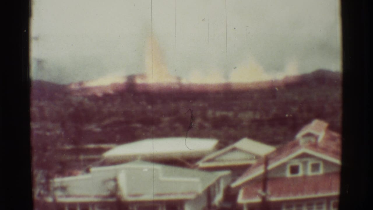 Distant fire glow and smoke appear beyond rooftops and hillside terrain.