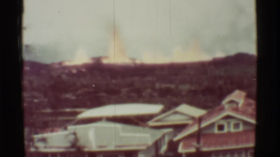 1971 Mauna Ulu frame showing smoke and fire glow over a hillside, with residential buildings in the foreground.