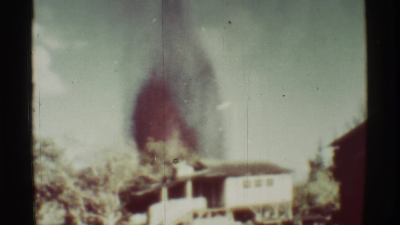 Smoke thickens above a pale low building and surrounding vegetation.