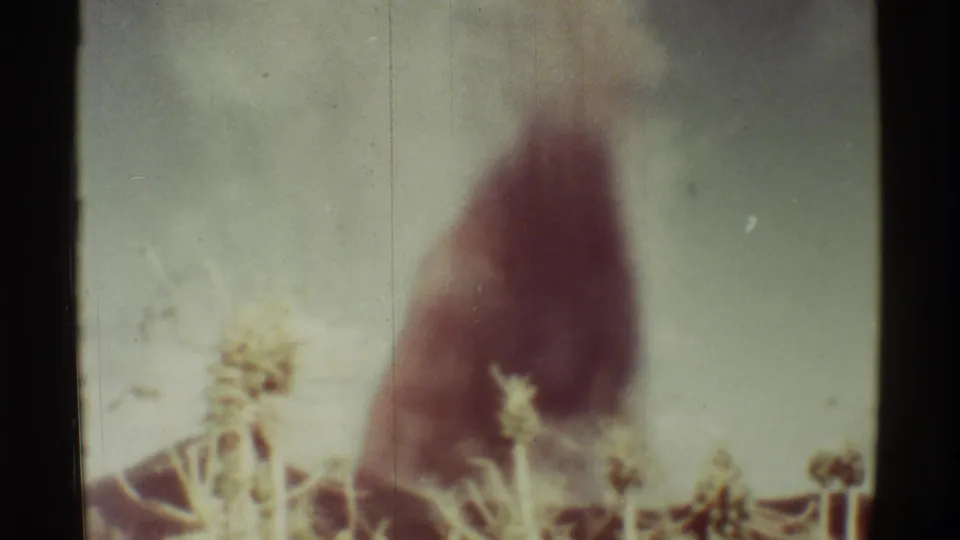 1971 Mauna Ulu, Hawaii 8mm frame showing a larger red-black smoke column above vegetation with part of a low structure visible.