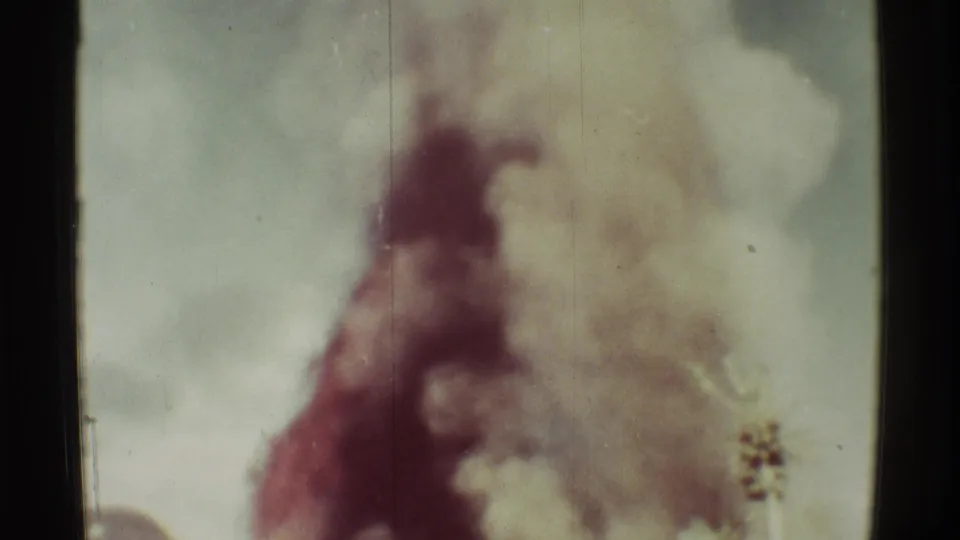 1971 Mauna Ulu, Hawaii home-movie still showing a large smoke column against a pale sky with a small plant head in the foreground.