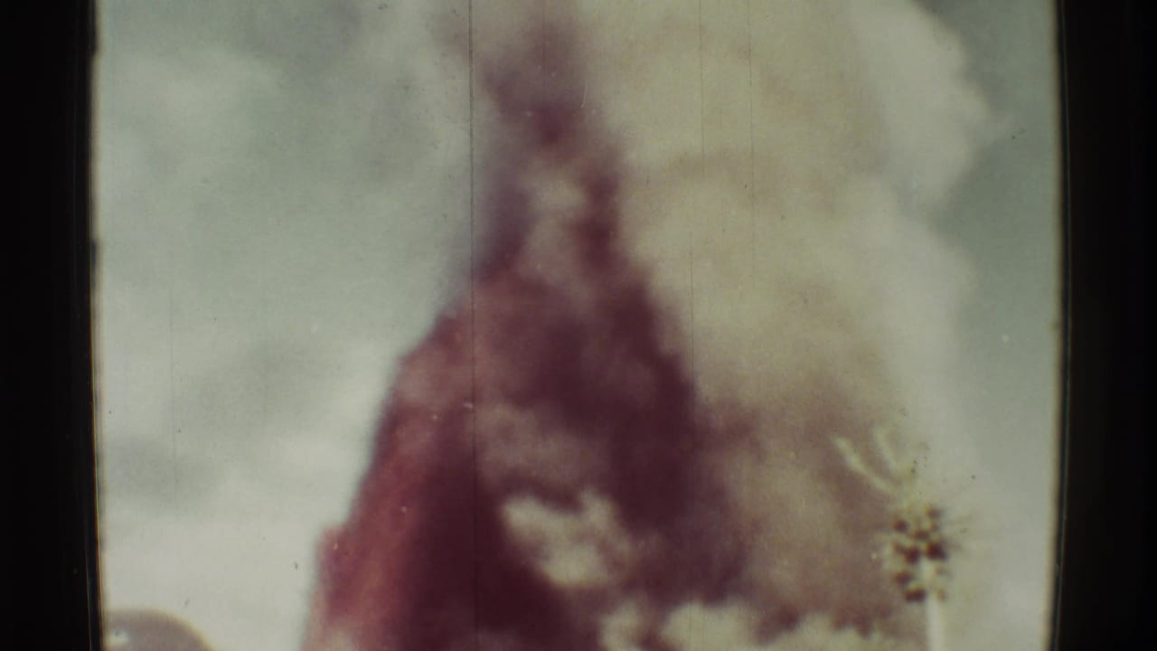 Tall dark smoke plume above a low building, with soft focus and film scratches.