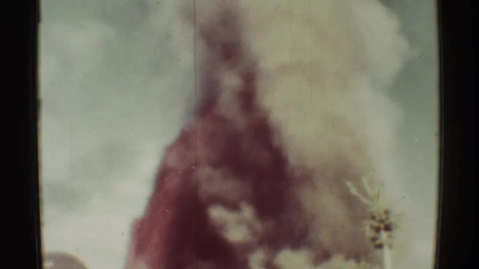 1971 Mauna Ulu eruption view with a dark plume rising behind a low building, recorded in faded small-gauge home-movie color.