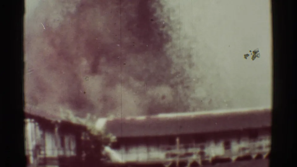 Faded 8mm view from Mauna Ulu, Hawaii, showing volcanic smoke behind a foreground roofline and small outdoor structures.