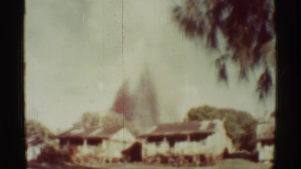 1971 Mauna Ulu, Hawaii 8mm frame showing smoke or dust behind low roofs, with tree branches and faded color.
