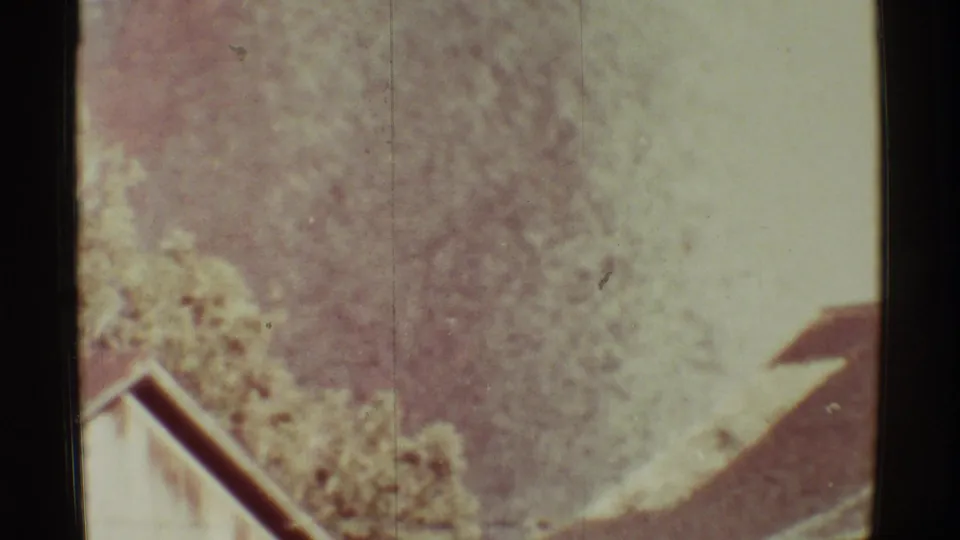 1971 Mauna Ulu home-movie frame with soft foliage, a roof edge, and pale volcanic haze in faded 8mm color.