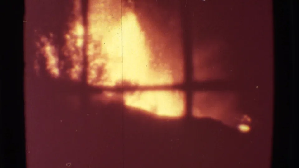 1971 Mauna Ulu 8mm frame showing orange volcanic glow partly obscured by branches and a dark foreground structure.