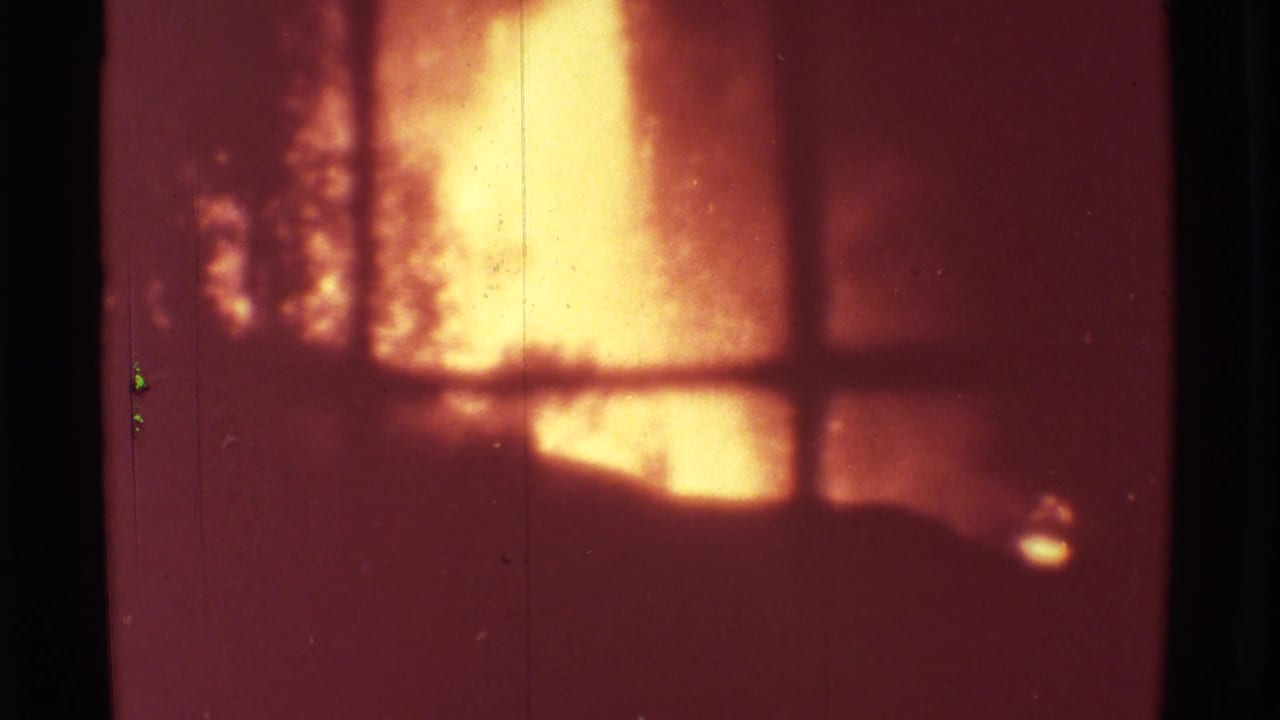 Bright lava glow seen through a dark window grid on reddish 8mm film.