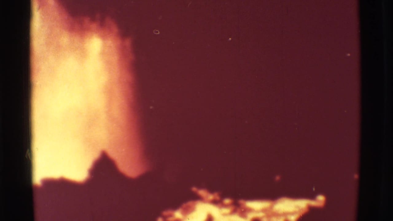 Bright volcanic plume and glowing lava against a dark red-orange sky on grainy 8mm film.