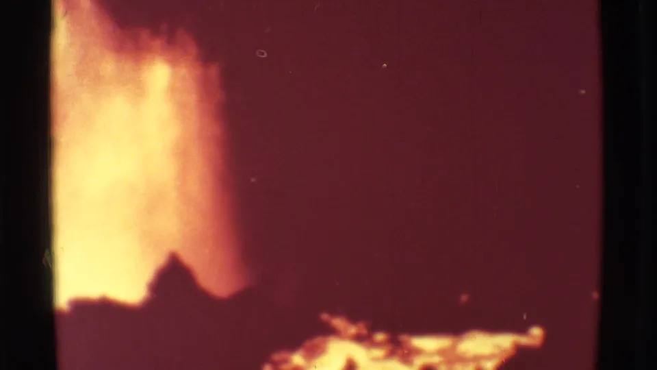 1971 Mauna Ulu, Hawaii 8mm frame showing a bright eruption plume rising behind dark volcanic ground with glowing lava at the lower edge.