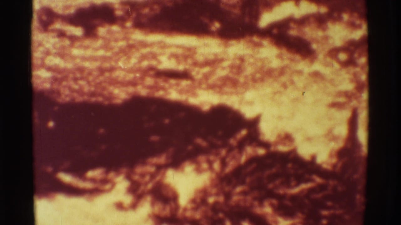 1971 Mauna Ulu 8mm frame with incandescent lava patches, dark cooled crust, and visible film grain across the volcanic surface.
