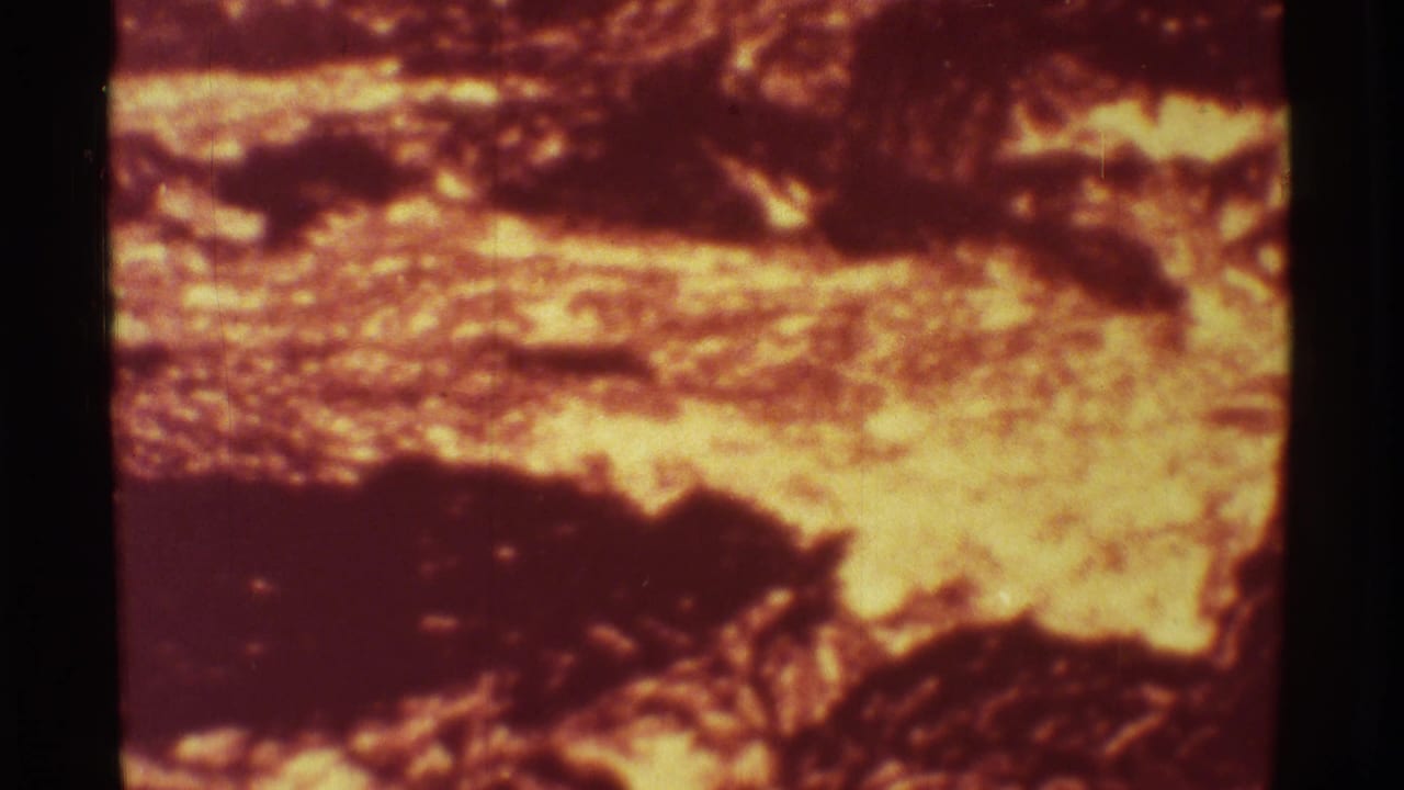 1971 Mauna Ulu 8mm frame showing a soft, grainy close-up of lava flow with glowing orange bands and dark crusted sections.