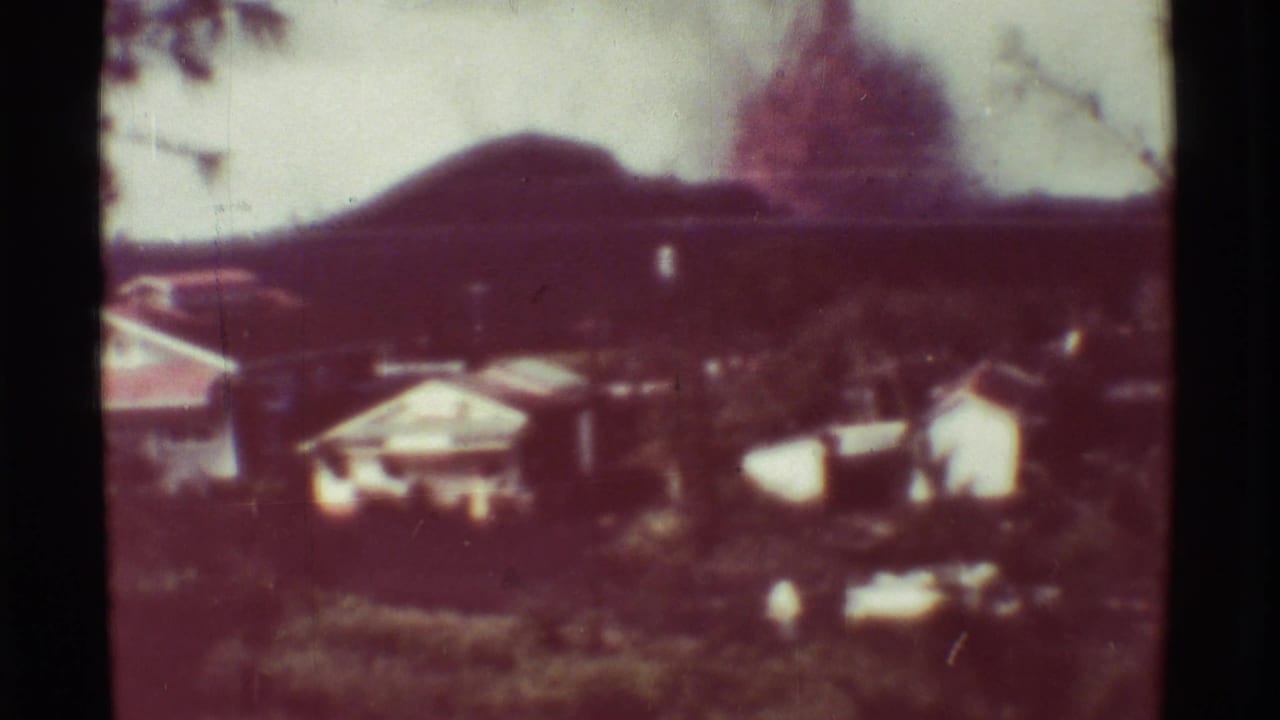 1971 Mauna Ulu, Hawaii 8mm view of buildings and vegetation beneath a hazy mountain slope after the fire scene.