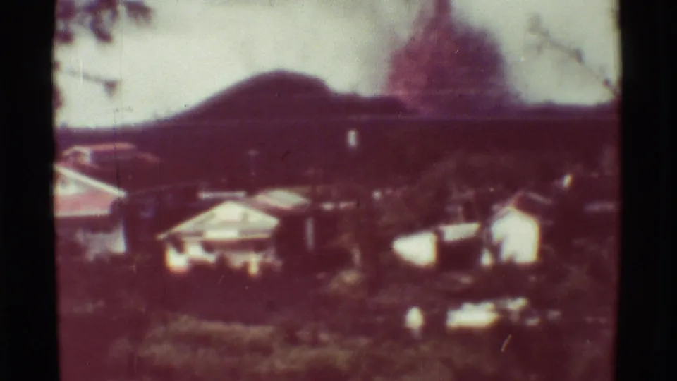 1971 Mauna Ulu, Hawaii 8mm view of buildings and vegetation beneath a hazy mountain slope after the fire scene.