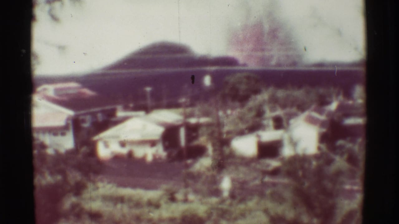 1971 Mauna Ulu, Hawaii frame showing a distant settlement, dense greenery, and a hazy mountain profile in faded 8mm color.