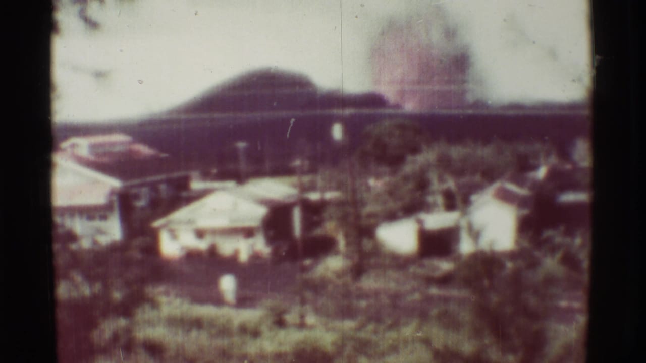 Similar distant view of plume, rooftops, vegetation, and dark film borders.