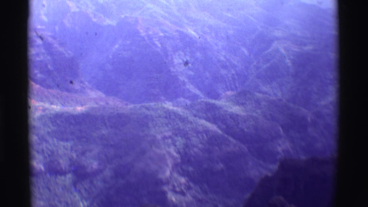 Purple-tinted aerial view of rugged mountain ridges and valleys framed by dark film borders.