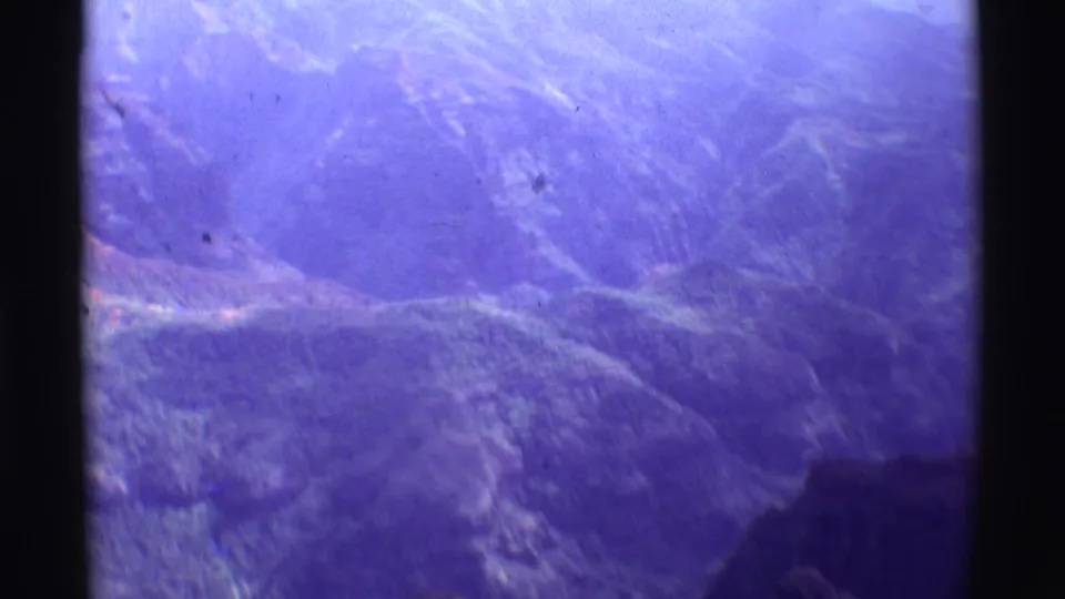 1971 8mm aerial view over Mauna Ulu, Hawaii, showing hazy ridges and valleys with strong purple film fading.