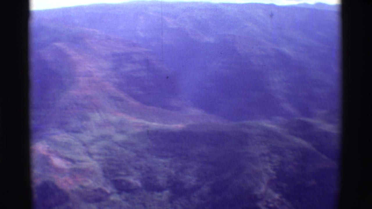 Hazy aerial landscape with layered slopes, pale sky, and dark vertical film-frame edge.