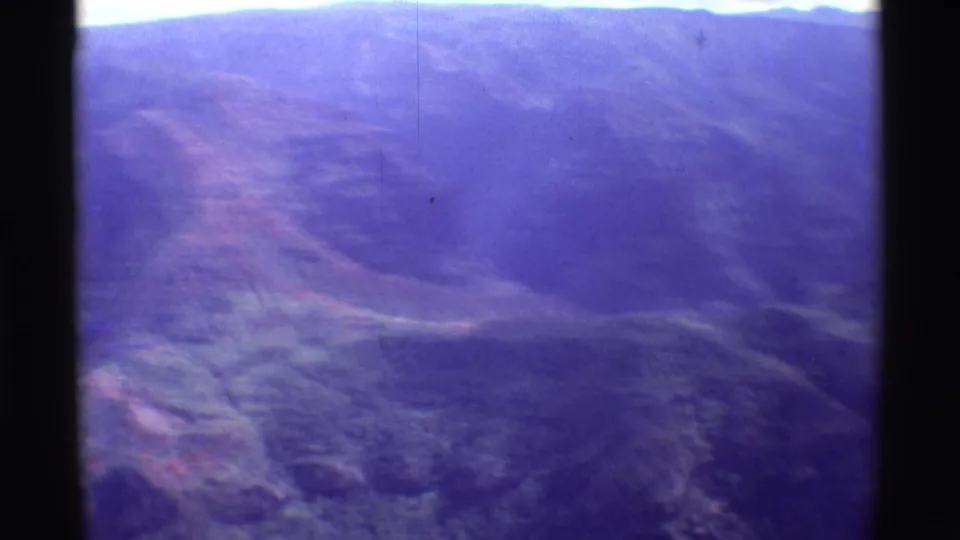 Aerial 8mm view of Mauna Ulu terrain with layered ridges, muted valley detail, and purple aging across the frame.