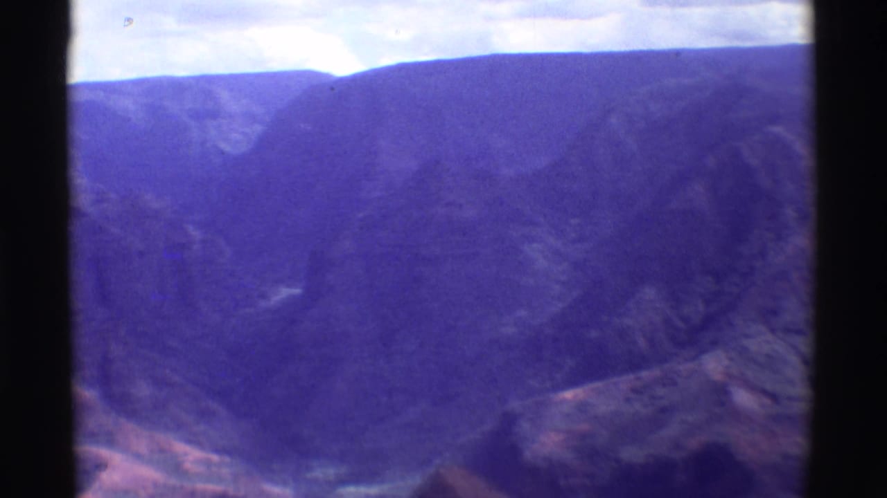 Aerial 8mm frame from Mauna Ulu, Hawaii, showing dark volcanic ridges, valley shapes, and visible film wear.