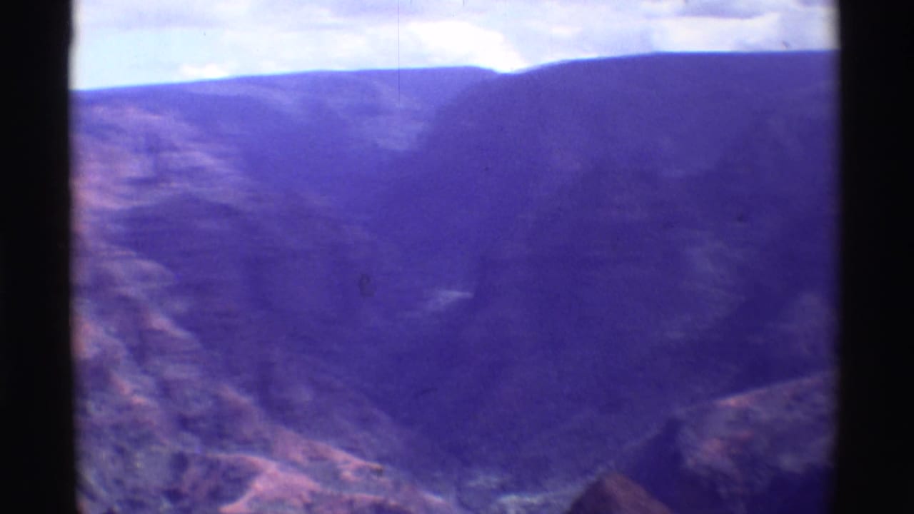 Purple-tinted canyon landscape with dark film borders and a bright sky above the ridgeline.